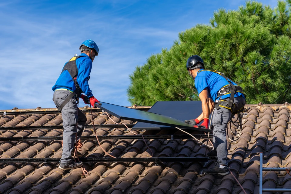 Technicien en combinaison verte installant ou entretenant des panneaux solaires photovoltaïques sur toiture, portant gants de protection, utilisant outil de serrage sur système de fixation