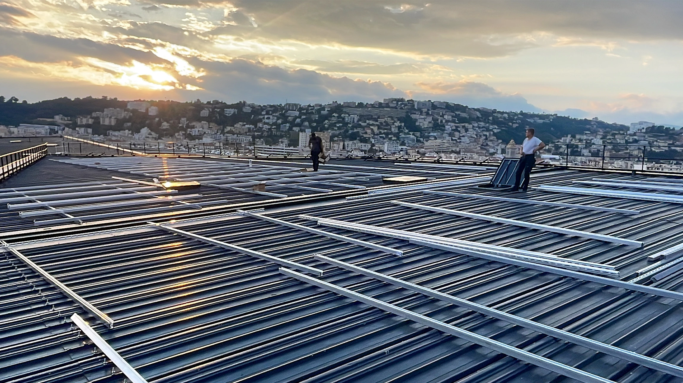 Vue aérienne d'un bâtiment commercial équipé de panneaux solaires photovoltaïques sur toiture bleue ondulée, au coucher du soleil